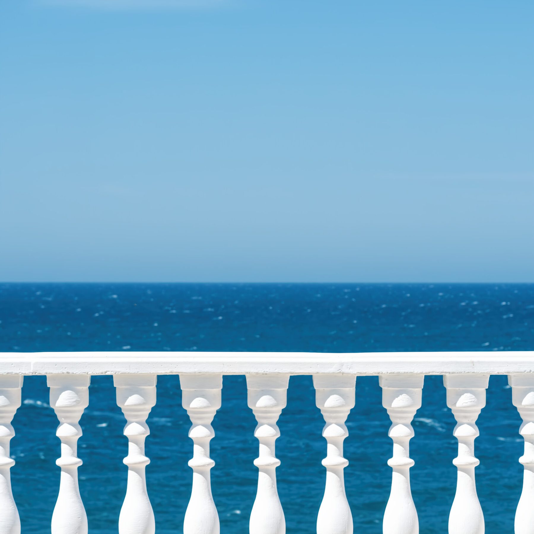 Classic roman white concrete railing outside the building on the terrace or promenade overlooking the sea with blue sky and clouds on the background. Close-up, with copy space.